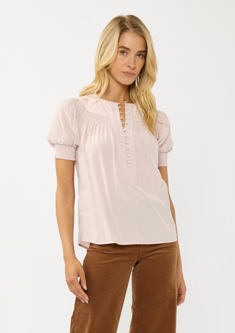 [Color: Rosewater] A front facing image of a blonde model wearing a light pink puff sleeve top with smocked cuffs and button front. A sweet and soft pink top for the office and casual outings. 
