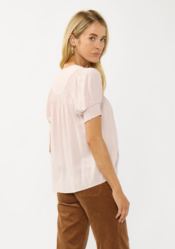 [Color: Rosewater] A side facing image of a blonde model wearing a light pink puff sleeve top with smocked cuffs and button front. A sweet and soft pink top for the office and casual outings. 