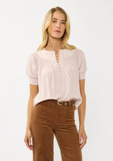 [Color: Rosewater] A front facing image of a blonde model wearing a light pink puff sleeve top with smocked cuffs and button front. A sweet and soft pink top for the office and casual outings. 