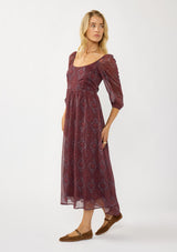 [Color: Wine/Rose] A side facing image of a blonde model wearing a floral diamond print chiffon maxi dress with metallic threads, a tie back, 3/4 sleeves, and a scoop neckline. A flattering special occasion dress for weddings or holidays. 