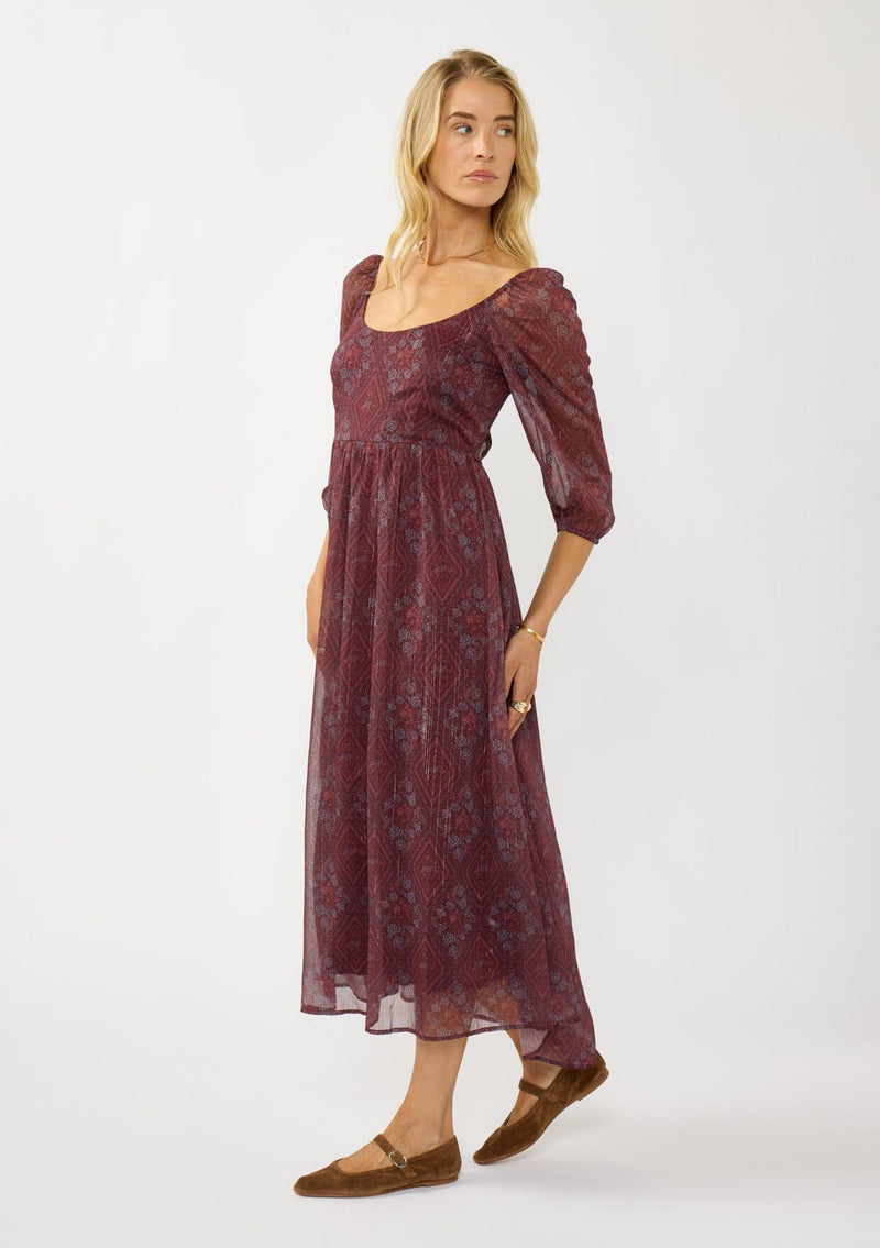 [Color: Wine/Rose] A side facing image of a blonde model wearing a floral diamond print chiffon maxi dress with metallic threads, a tie back, 3/4 sleeves, and a scoop neckline. A flattering special occasion dress for weddings or holidays. 