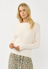 [Color: Natural] A front facing image of a blonde model wearing an off white waffle knit pullover sweater. With long sleeves, a relaxed fit, and a wide neckline that can be worn off the shoulder.