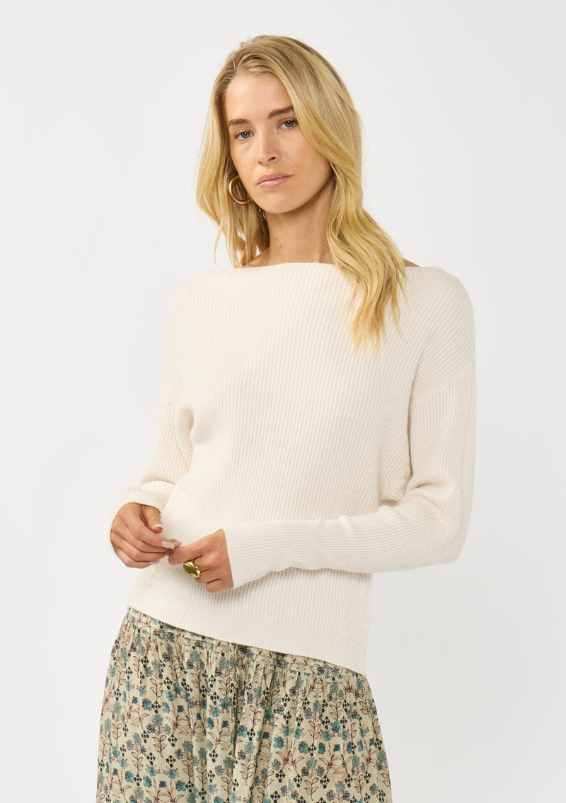 [Color: Natural] A front facing image of a blonde model wearing an off white waffle knit pullover sweater. With long sleeves, a relaxed fit, and a wide neckline that can be worn off the shoulder.