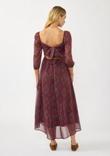 [Color: Wine/Rose] A back facing image of a blonde model wearing a floral diamond print chiffon maxi dress with metallic threads, a tie back, 3/4 sleeves, and a scoop neckline. A flattering special occasion dress for weddings or holidays. 