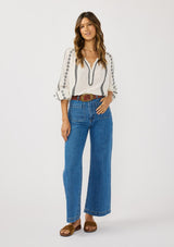 [Color: White/Black] A front facing image of a brunette model wearing a white cotton top with black embroidered details. A classic boho top with a split v-neckline, button front, and long sleeves.  