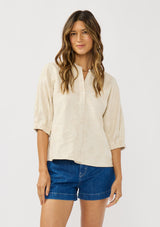 [Color: Natural] A front facing image of a brunette model wearing a beige linen-blend top featuring jacquard detailing, a button-front closure, and elbow-length sleeves with elasticized cuffs.