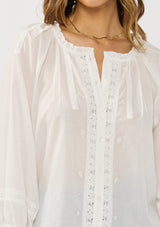 [Color: White] A detail image of a brunette model wearing a white sheer blouse with lace trims. Featuring a round neckline, button front, and 33/4 length sleeves with elastic cuffs. A lightweight boho cotton blouse. 