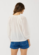 [Color: White] A back facing image of a brunette model wearing a white sheer blouse with lace trims. Featuring a round neckline, button front, and 33/4 length sleeves with elastic cuffs. A lightweight boho cotton blouse. 