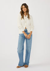 [Color: White] A front facing image of a brunette model wearing a cable knit sweater with a button front. Effortless and easy to style, featuring a classic ribbed trim and crew neckline. A classic year round sweater with a cozy fit. 