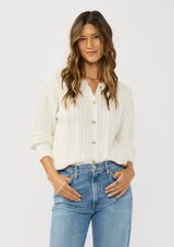 [Color: White] A front facing image of a brunette model wearing a cable knit sweater with a button front. Effortless and easy to style, featuring a classic ribbed trim and crew neckline. A classic year round sweater with a cozy fit. 