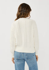 [Color: White] A back facing image of a brunette model wearing a cable knit sweater with a button front. Effortless and easy to style, featuring a classic ribbed trim and crew neckline. A classic year round sweater with a cozy fit. 