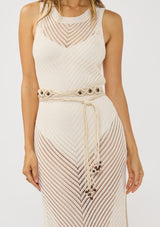 [Color: Ivory] A brunette model wearing a crochet dress with a long bohemian macrame belt with beads wrapped around the dress. 