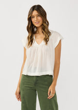 [Color: White] A front facing image of a brunette model wearing a flowy white bohemian top with short sleeves, a v-neckline, raw trim edges, and a shirred yoke. 