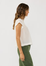 [Color: White] A side facing image of a brunette model wearing a flowy white bohemian top with short sleeves, a v-neckline, raw trim edges, and a shirred yoke. 