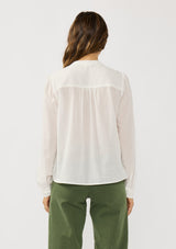 [Color: White] A back facing image of a brunette model wearing a white blouse with lace details, button front, and button cuffs. 