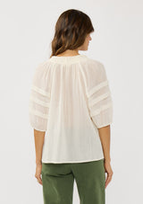 [Color: Ivory] A back facing image of a brunette model wearing an ivory sheer top with a split v-neckline and elbow length sleeves with pleats. A casual warm weather top for resort season. 