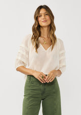 [Color: Ivory] A front facing image of a brunette model wearing an ivory sheer top with a split v-neckline and elbow length sleeves with pleats. A casual warm weather top for resort season. 