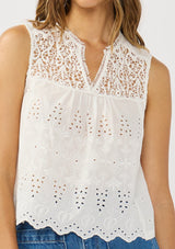 [Color: White] A detail image of a brunette model wearing a white tank top with lace and eyelet detailing. 