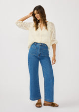 [Color: Natural] A front facing image of a brunette model wearing a sheer lace blouse with floral embroidery. Featuring a classic button up design, split v-neckline, and long sleeves. A breezy top with no lining for warm weather styling. 