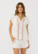 [Color: White/Dusty Rose] A front facing image of a brunette model wearing a white short sleeve top with pink embroidery, lace inserts, and a split v-neckline. Styled with matching bottoms. 