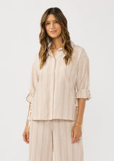 [Color: Sand/White] A front facing image of a brunette model wearing a striped shirt with a collared neckline, button front, roll tab sleeves, and a playful side tie detail. 