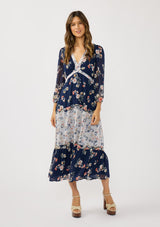 [Color: Navy/Coral] A front facing image of a brunette model wearing a navy floral dress with an empire waist, v-neckline, long sleeves, and a tiered flowy skirt. A feminine flowy chiffon dress for the spring season. 