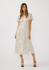 [Color: Natural/Dusty Peach] A front facing image of a brunette model wearing a dotted floral chiffon midi dress with clipped lurex for a touch of sparkle. Featuring a flattering v-neckline, short flutter sleeves, and an elastic waist at the back. 