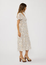 [Color: Natural/Dusty Peach] A side facing image of a brunette model wearing a dotted floral chiffon midi dress with clipped lurex for a touch of sparkle. Featuring a flattering v-neckline, short flutter sleeves, and an elastic waist at the back. 