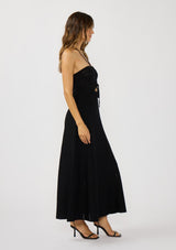 [Color: Black] A side facing image of a brunette model wearing a black knit halter dress with pointelle detail. Featuring a chic halter neckline, ruched bust with adjustable ties, and a front cutout. 