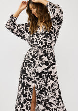 [Color: Vanilla/Black] A front facing image of a brunette model wearing an abstract floral print maxi dress with long dolman sleeves, a v-neckline, and long waist ties for multiple ways to style. Complete with a chic front slit for movement. 