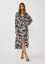 [Color: Vanilla/Black] A front facing image of a brunette model wearing an abstract floral print maxi dress with long dolman sleeves, a v-neckline, and long waist ties for multiple ways to style. Complete with a chic front slit for movement. 