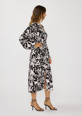 [Color: Vanilla/Black] A side facing image of a brunette model wearing an abstract floral print maxi dress with long dolman sleeves, a v-neckline, and long waist ties for multiple ways to style. Complete with a chic front slit for movement. 
