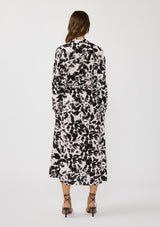 [Color: Vanilla/Black] A back facing image of a brunette model wearing an abstract floral print maxi dress with long dolman sleeves, a v-neckline, and long waist ties for multiple ways to style. Complete with a chic side slit for movement. 