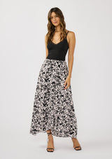 [Color: Vanilla/Black] A front facing image of a brunette model wearing a black and white floral print skirt with a subtle pink tint, featuring long waist ties for an effortless wrap silhouette and a chic side tie. Lightweight and flowy, perfect for vacation or everyday wear.