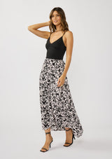 [Color: Vanilla/Black] A side facing image of a brunette model wearing a black and white floral print skirt with a subtle pink tint, featuring long waist ties for an effortless wrap silhouette and a chic side tie. Lightweight and flowy, perfect for vacation or everyday wear.