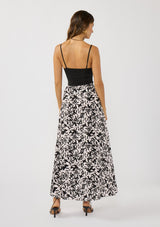 [Color: Vanilla/Black] A back facing image of a brunette model wearing a black and white floral print skirt with a subtle pink tint, featuring long waist ties for an effortless wrap silhouette and a chic side tie. Lightweight and flowy, perfect for vacation or everyday wear.
