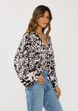 [Color: Vanilla/Black] A side facing image of a brunette model wearing a abstract floral kimono top with  an adjustable tie front and long billowy sleeves. 