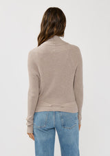 [Color: Heather Cement] A photo of a Lovestitch model wearing a chic beige waffle knit wrap front sweater with long sleeves, a v neckline, and a button closure at the back. The long ties can be styled in multiple ways.