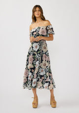 [Color: Black/Blush] A front facing image of a brunette model wearing a black and pink floral chiffon midi dress with an elastic off shoulder, braided waist belt, and tiered flowy skirt. A floral dress for brunch, spring styling, and special occasions. 