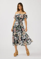 [Color: Black/Blush] A front facing image of a brunette model wearing a black and pink floral chiffon midi dress with an elastic off shoulder, braided waist belt, and tiered flowy skirt. A floral dress for brunch, spring styling, and special occasions. 