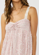 [Color: Vanilla/Rose] A detail image of a brunette model wearing a pink floral bohemian maxi dress with a flowy tiered silhouette, crochet adjustable straps, a ruched bust detail, and ruffle trim accents. A pretty beach dress for vacation. 