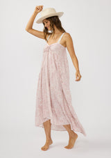 [Color: Vanilla/Rose] A side facing image of a brunette model wearing a pink floral bohemian maxi dress with a flowy tiered silhouette, crochet adjustable straps, a ruched bust detail, and ruffle trim accents. A pretty beach dress for vacation. 