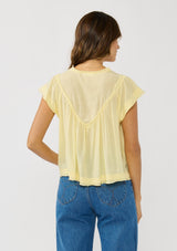 [Color: Yellow] A back facing image of a brunette model wearing a flowy yellow bohemian top with short sleeves, a v-neckline, raw trim edges, and a shirred yoke. 