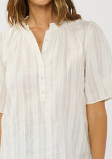 [Color: White] A detail image of a brunette model wearing a white button up puff sleeve top with a jacquard stripe and  metallic thread details. 