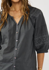[Color: Grey] A detail image of a brunette model wearing bohemian grey embroidered blouse with 3/4 length sleeves and a decorative button front. 
