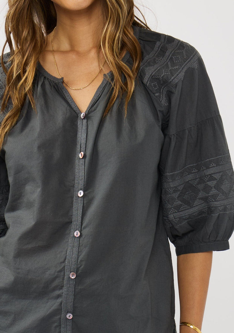 [Color: Grey] A detail image of a brunette model wearing bohemian grey embroidered blouse with 3/4 length sleeves and a decorative button front. 