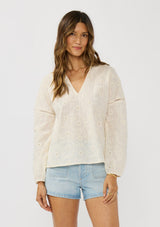 [Color: Tea Dye] A front facing image of a brunette model wearing a tonal embroidered blouse with a collared v-neckline and long sleeves with elastic cuffs. A breezy cotton blouse for casual settings. 
