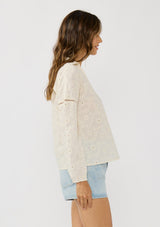 [Color: Tea Dye] A side facing image of a brunette model wearing a tonal embroidered blouse with a collared v-neckline and long sleeves with elastic cuffs. A breezy cotton blouse for casual settings. 