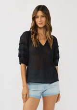 [Color: Black] A front facing image of a brunette model wearing an black sheer top with a split v-neckline and elbow length sleeves with pleats. A casual warm weather top for resort season. 
