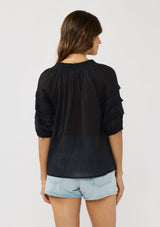 [Color: Black] A back facing image of a brunette model wearing an black sheer top with a split v-neckline and elbow length sleeves with pleats. A casual warm weather top for resort season. 